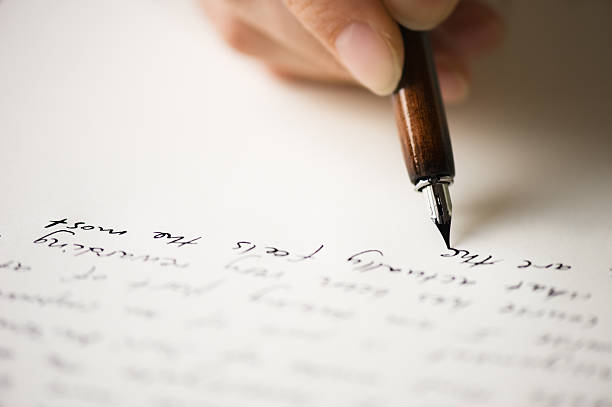 Il s'agit d'une page blanche sur laquelle sont écrit des mots à la plume. on voit également une main tenir un stylo plume.