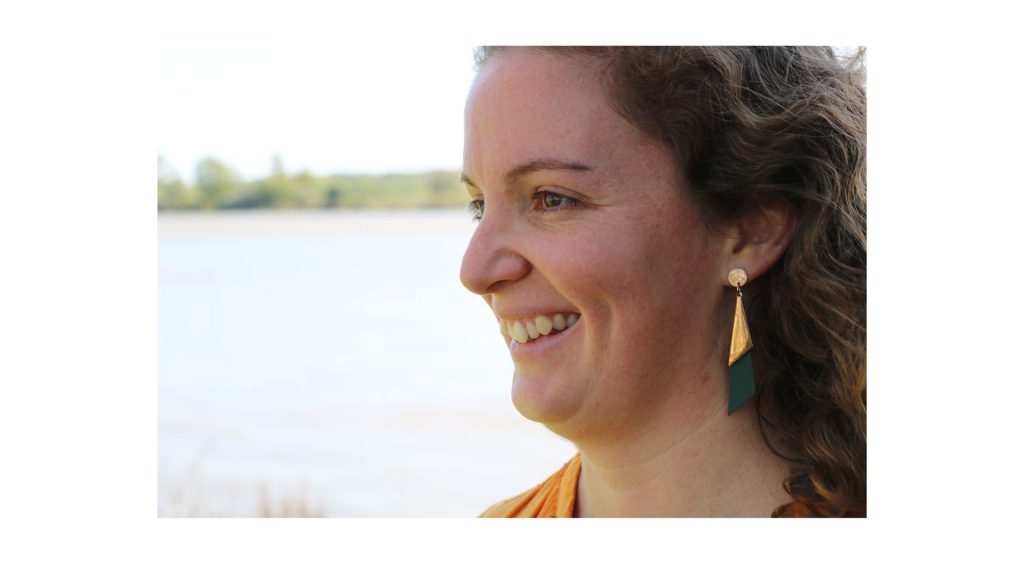 Il s'agit d'une photo d'un visage d'une femme, souriante, de profil. En second plan un distingue une rivière.
