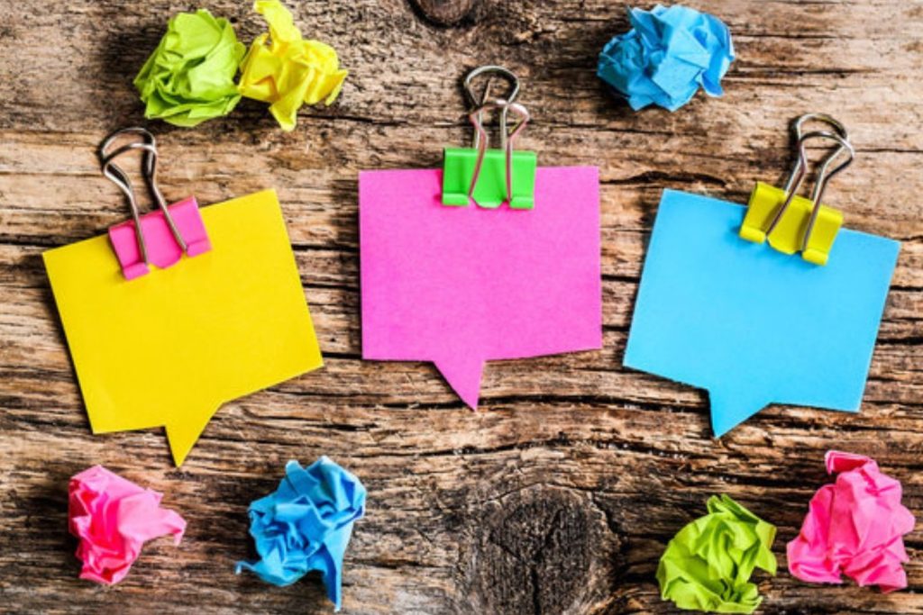sur une table en bois brut, sur 3 ligne il y a des boulettes de papier colorées, sur la ligne du milieu, il y a 3 post-it colorés retenus chacun par une pince